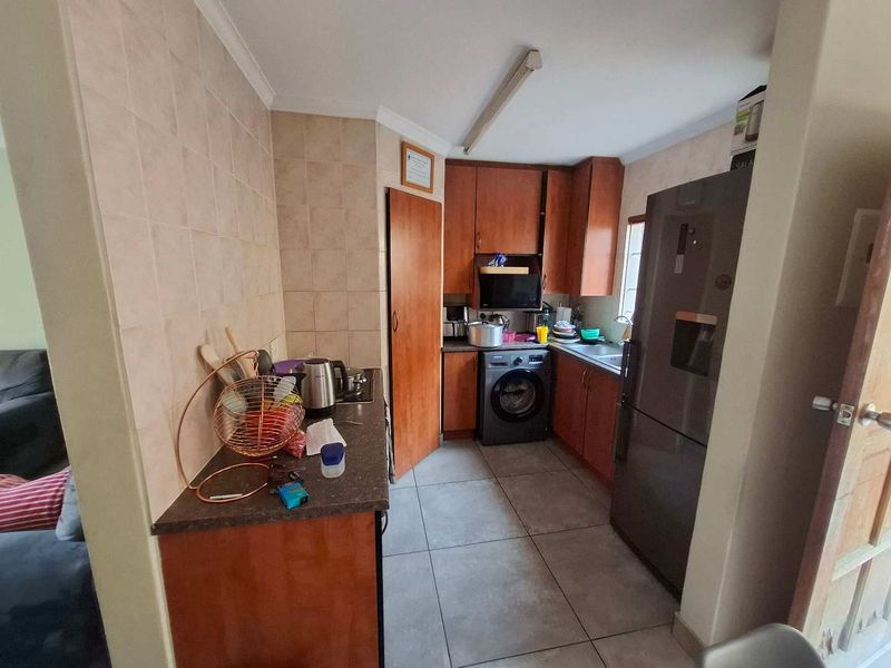 Compact kitchen featuring wooden cabinetry, tiled backsplash, laminate countertops, and integrated laundry plumbing, offering a functional layout with potential for modern updates.