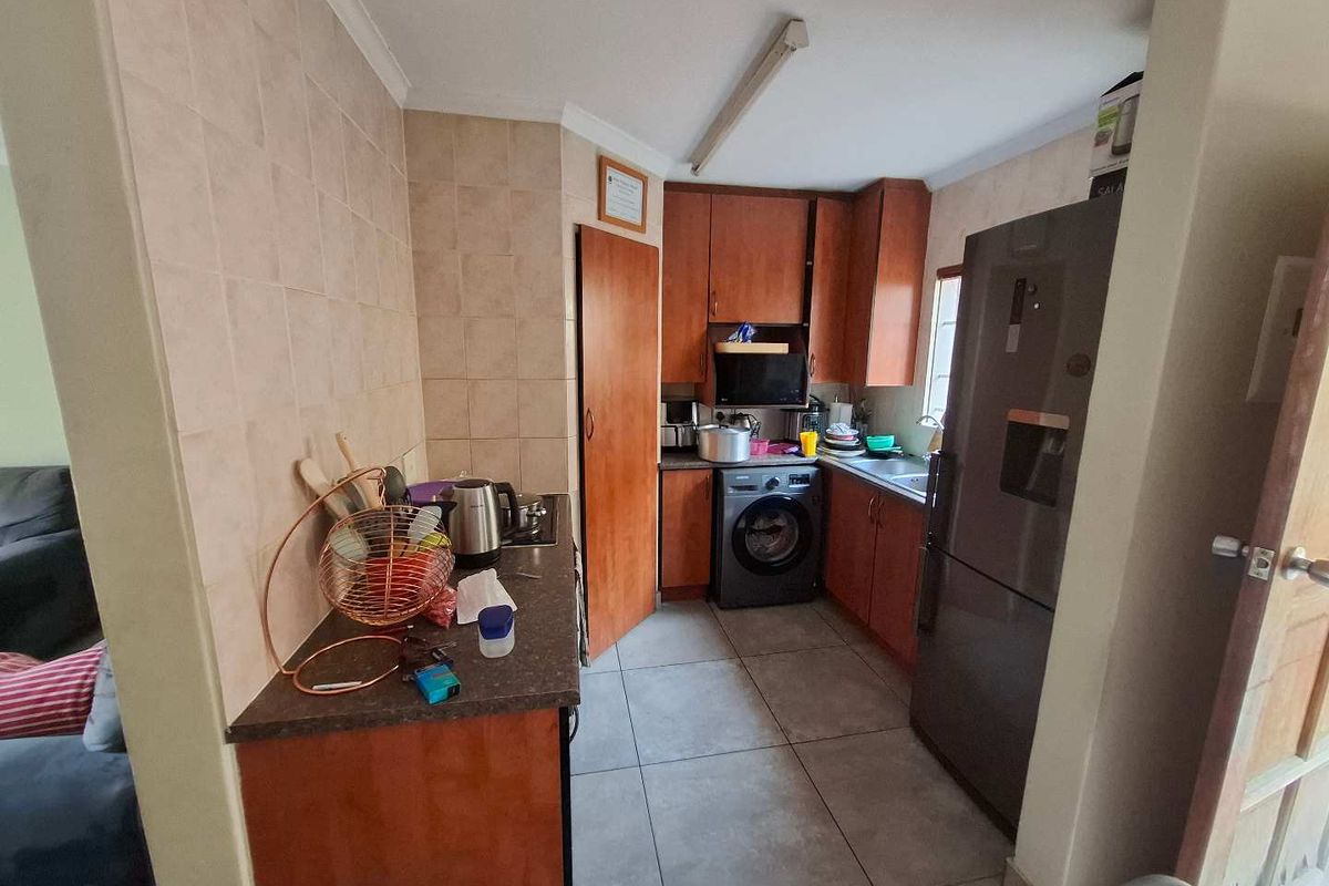 Compact kitchen featuring wooden cabinetry, tiled backsplash, laminate countertops, and integrated laundry plumbing, offering a functional layout with potential for modern updates.