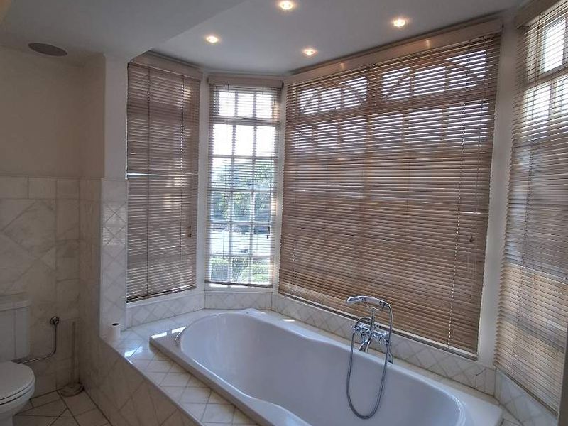 A bright bathroom featuring a built-in bathtub set within a bay window area, complemented by tiled flooring and recessed ceiling lighting.