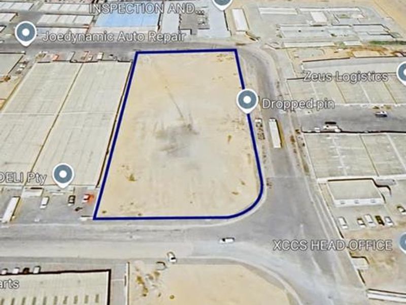 An aerial view of a vacant industrial plot situated within an established industrial park, featuring direct road access and surrounding commercial infrastructure.