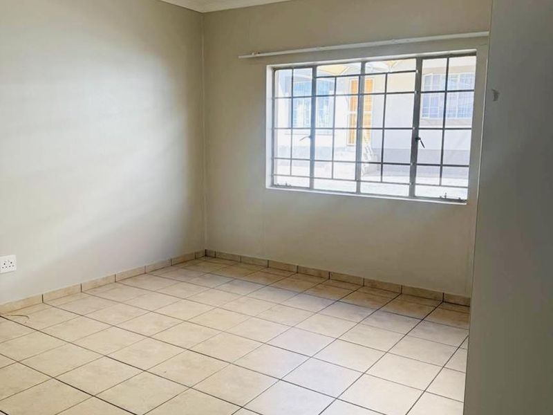 A vacant bedroom featuring neutral tiled flooring, a window with security bars, and a simple ceiling light fixture.