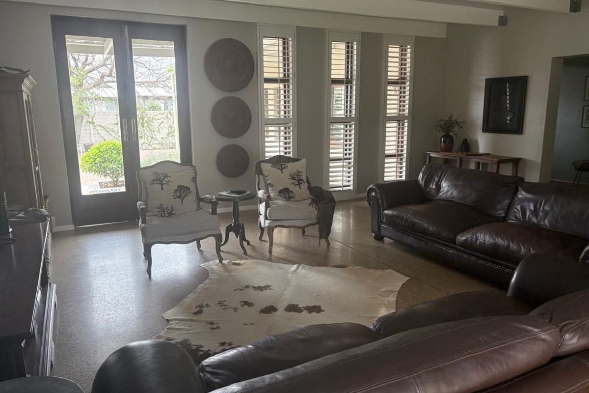 Spacious living room featuring polished concrete floors, exposed ceiling beams, and plantation shutters, with direct access to the outdoor patio area.