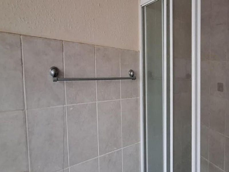 A bathroom featuring a shower enclosure with tiled walls and a fixed towel rail, showing signs of wear in the grout.