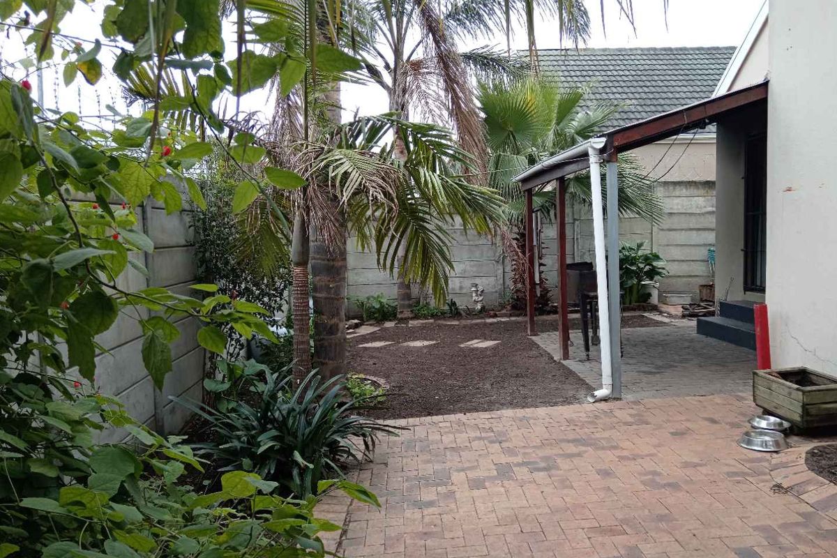 A rear garden area featuring a paved patio, a covered veranda, and established palm trees enclosed by precast concrete boundary walls.