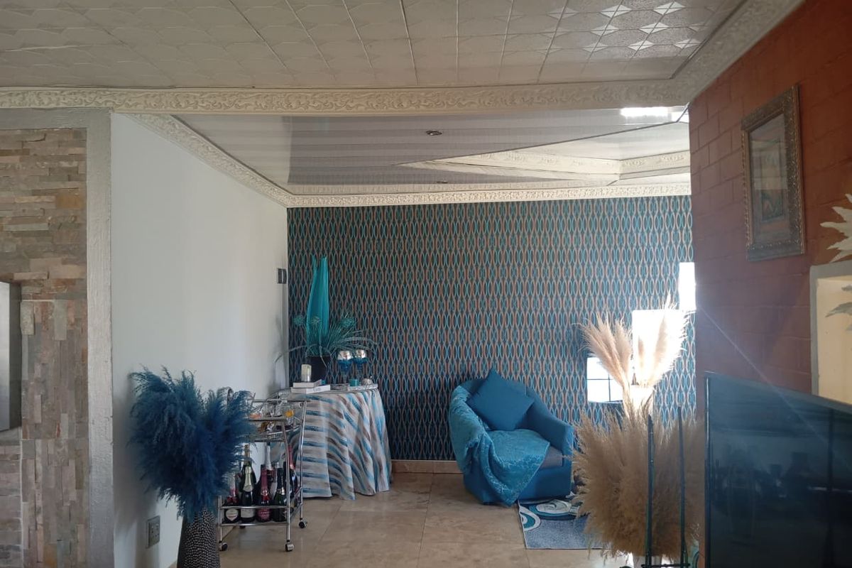 Living room featuring tiled flooring, a stone-clad feature wall, patterned wallpaper, and decorative ceiling tiles with ornate cornicing.
