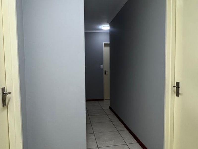 A clean and functional hallway featuring neutral grey walls, tiled flooring, and multiple internal doors providing access to various rooms.
