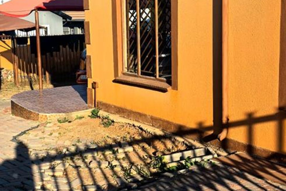 Side view of the house exterior featuring a tiled roof, security-barred window, and paved driveway area.