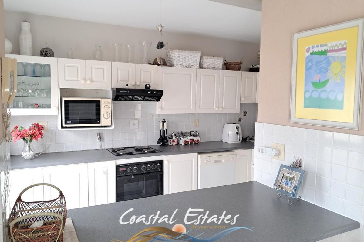 A functional kitchen featuring white cabinetry, a built-in oven, hob, extractor fan, and a breakfast bar with a grey laminate countertop.