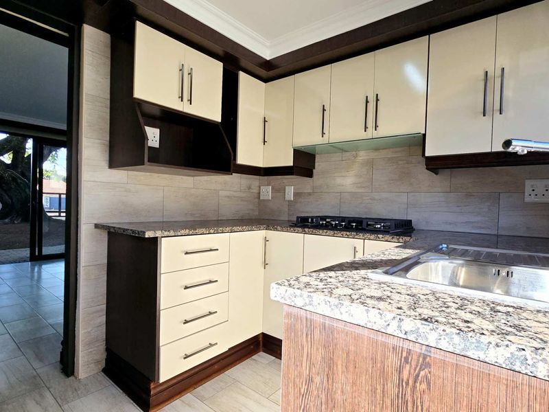 Modern kitchen featuring granite countertops, built-in cabinetry, a gas hob, and a stainless steel sink with a tiled backsplash.