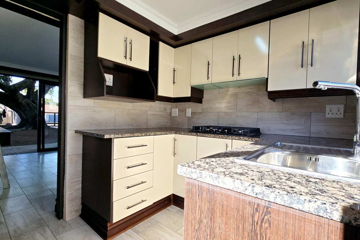 Modern kitchen featuring granite countertops, built-in cabinetry, a gas hob, and a stainless steel sink with a tiled backsplash.