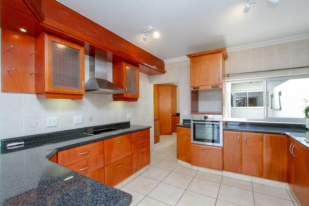 A well-maintained kitchen featuring wooden cabinetry, granite countertops, a built-in oven, and an electric hob with a stainless steel extractor fan.