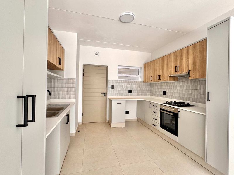 Modern kitchen featuring light wood-tone upper cabinets, white lower cabinetry, stone countertops, gas hob, electric oven, and a tiled backsplash.