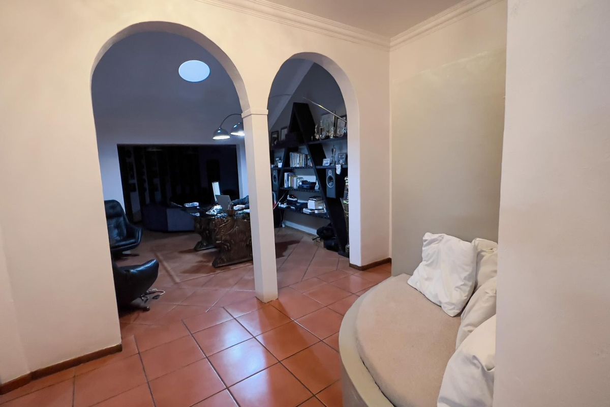 Spacious living area featuring distinctive arched doorways, terracotta floor tiles, and a skylight, creating a unique architectural flow between connected rooms.