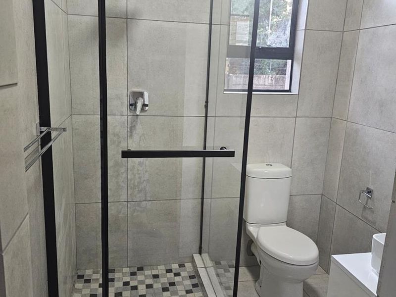 Modern bathroom featuring a walk-in shower with a black-framed glass enclosure, rainfall shower head, and neutral floor-to-ceiling tiling.