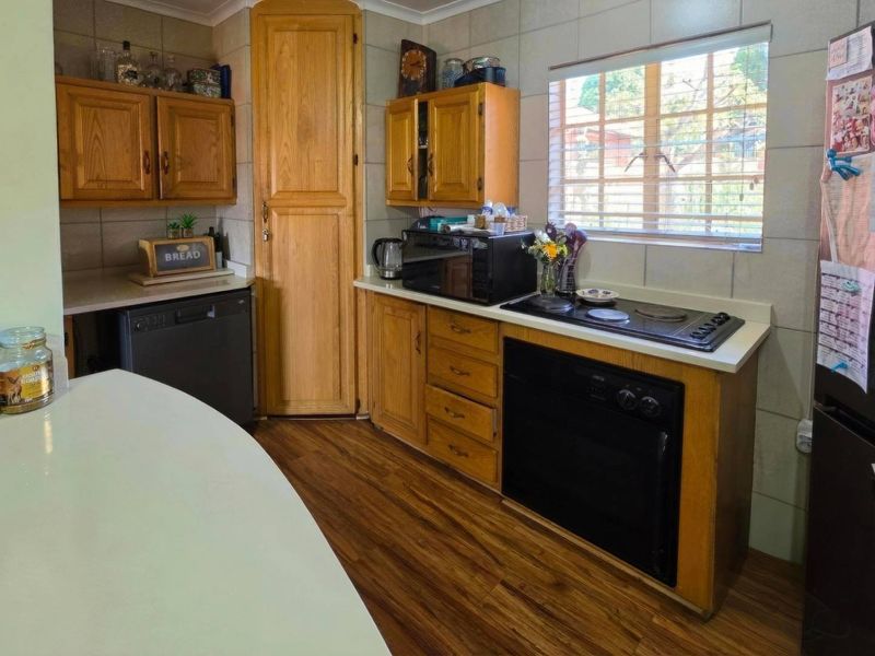 A functional kitchen featuring wooden cabinetry, a built-in oven, electric hob, and tiled backsplash, offering a classic layout with ample storage space.