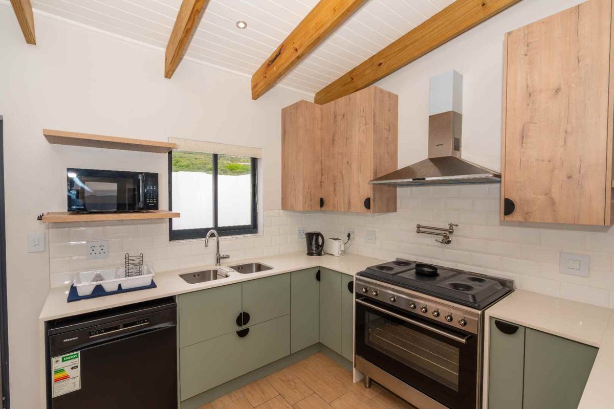 Modern kitchen featuring light green cabinetry, wood-look countertops, subway tile backsplash, exposed timber ceiling beams, and a stainless steel gas stove with extractor fan.