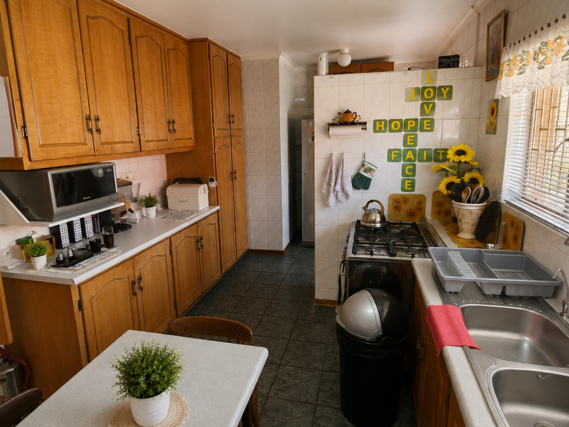 A functional kitchen featuring traditional wooden cabinetry, a gas hob, built-in oven, and a double stainless steel sink with tiled finishes throughout.
