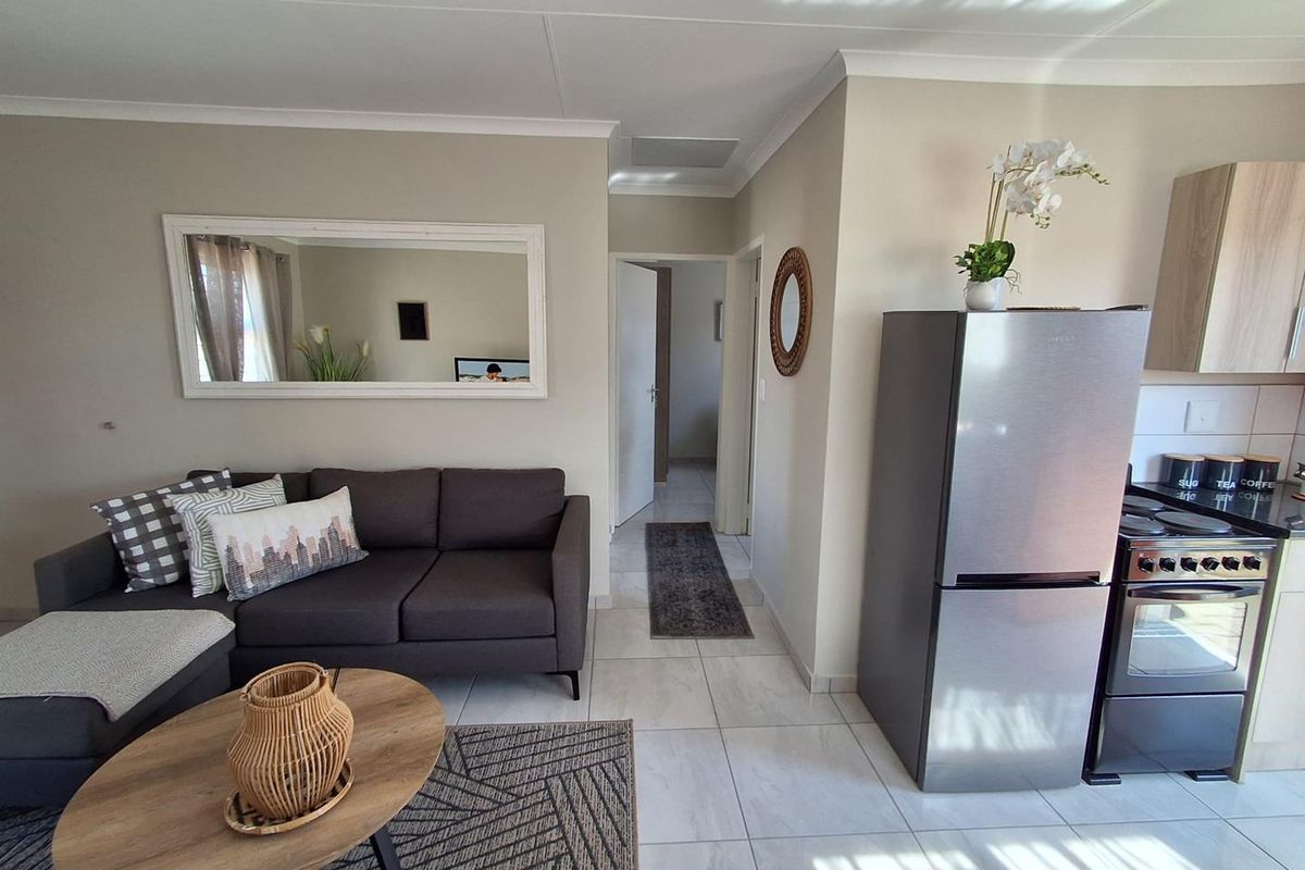 An open-plan living area featuring tiled flooring, neutral walls, and a compact kitchen space with modern cabinetry and a freestanding stove.