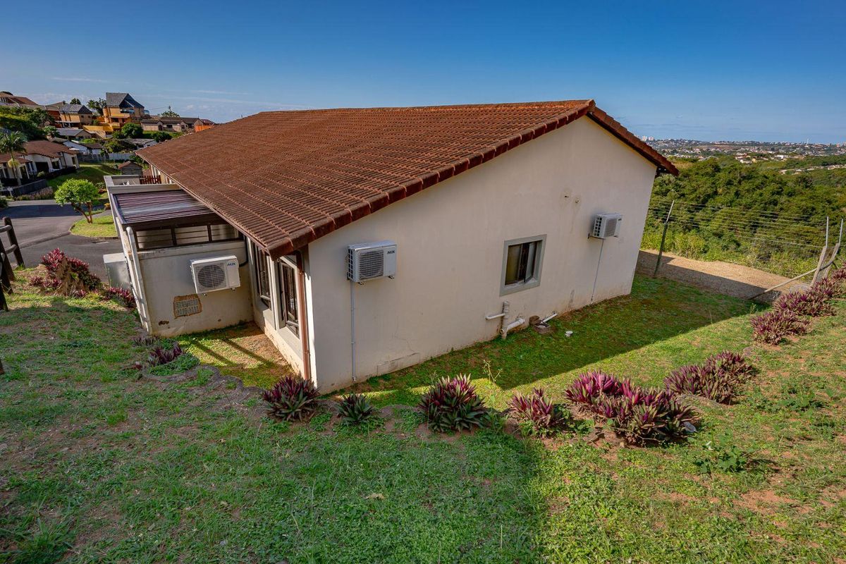 Rear exterior view of the townhouse featuring a tiled roof, mounted air conditioning units, and a sloped garden area with security fencing.