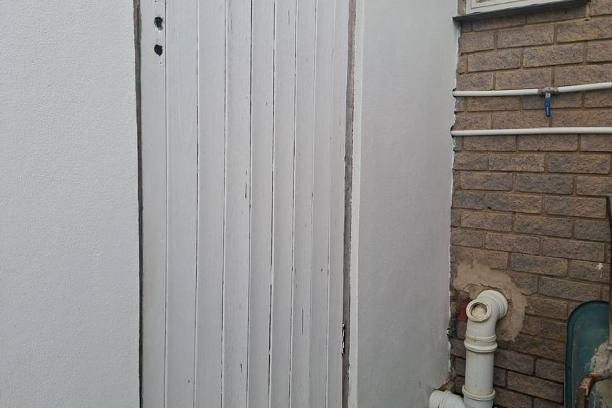 Exterior view of a utility access door with exposed plumbing and brickwork, showing signs of wear and maintenance requirements.