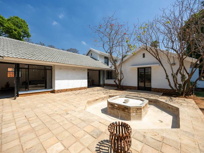 Spacious rear courtyard featuring a paved patio area, a central brick fountain, and direct access to the main house through large glass doors.