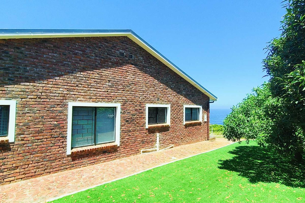 A side view of the brick-clad house exterior featuring a paved walkway, manicured lawn, and ocean views in the distance.