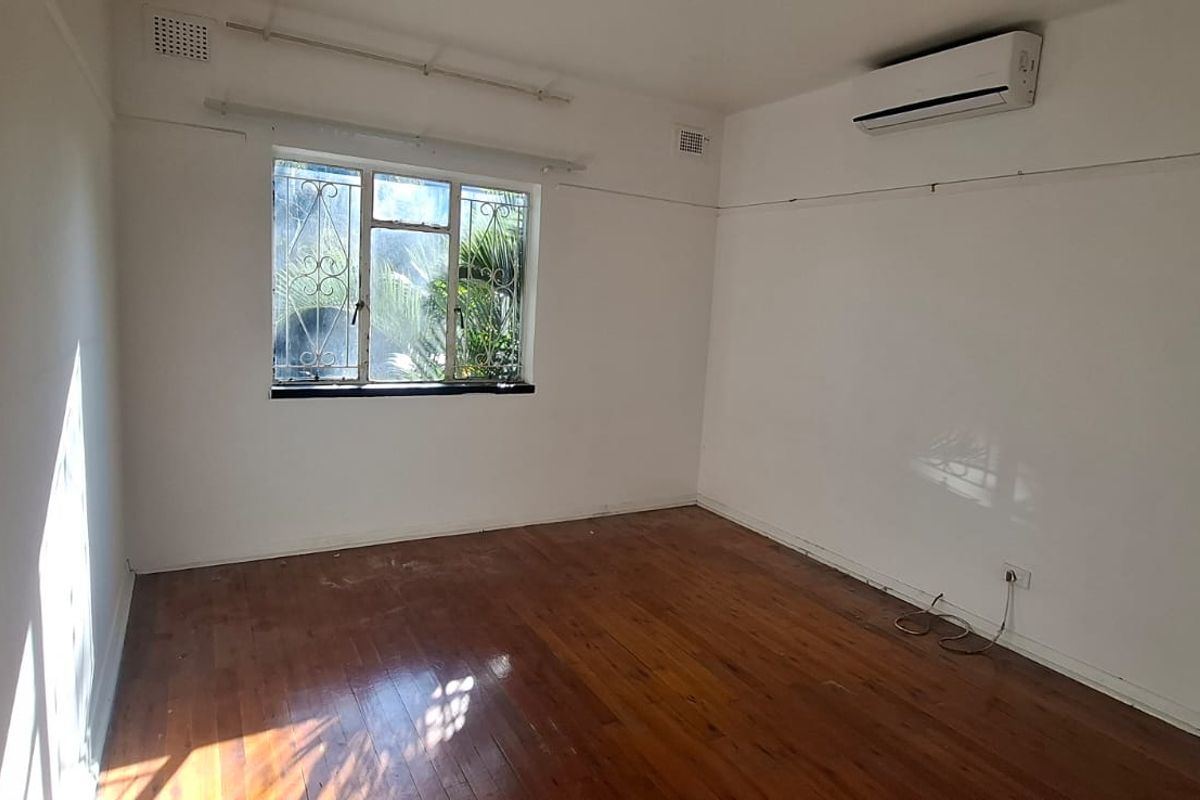 An empty bedroom featuring polished timber flooring, a wall-mounted split-system air conditioner, and a window with security bars.