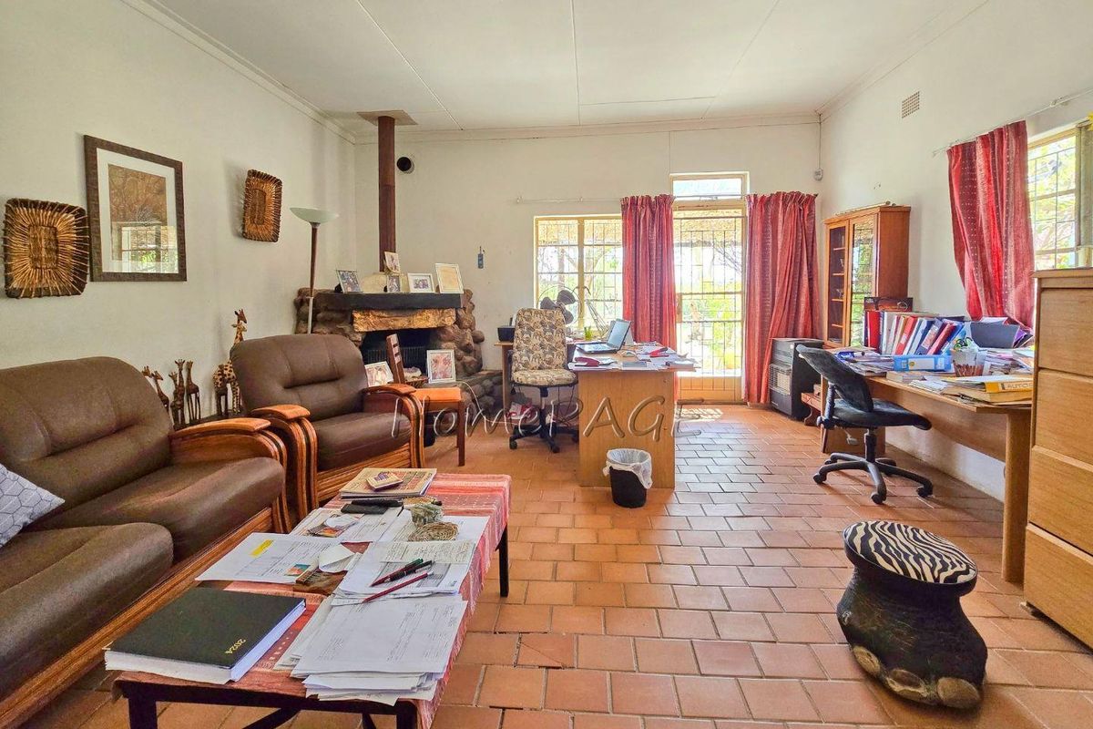 Spacious living area featuring a rustic stone fireplace, terracotta tiled flooring, and direct access to the garden through a glass-paneled door.