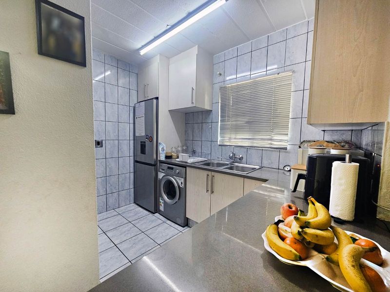 Functional kitchen featuring tiled walls and flooring, built-in cabinetry, a double basin sink, and space for integrated laundry appliances.