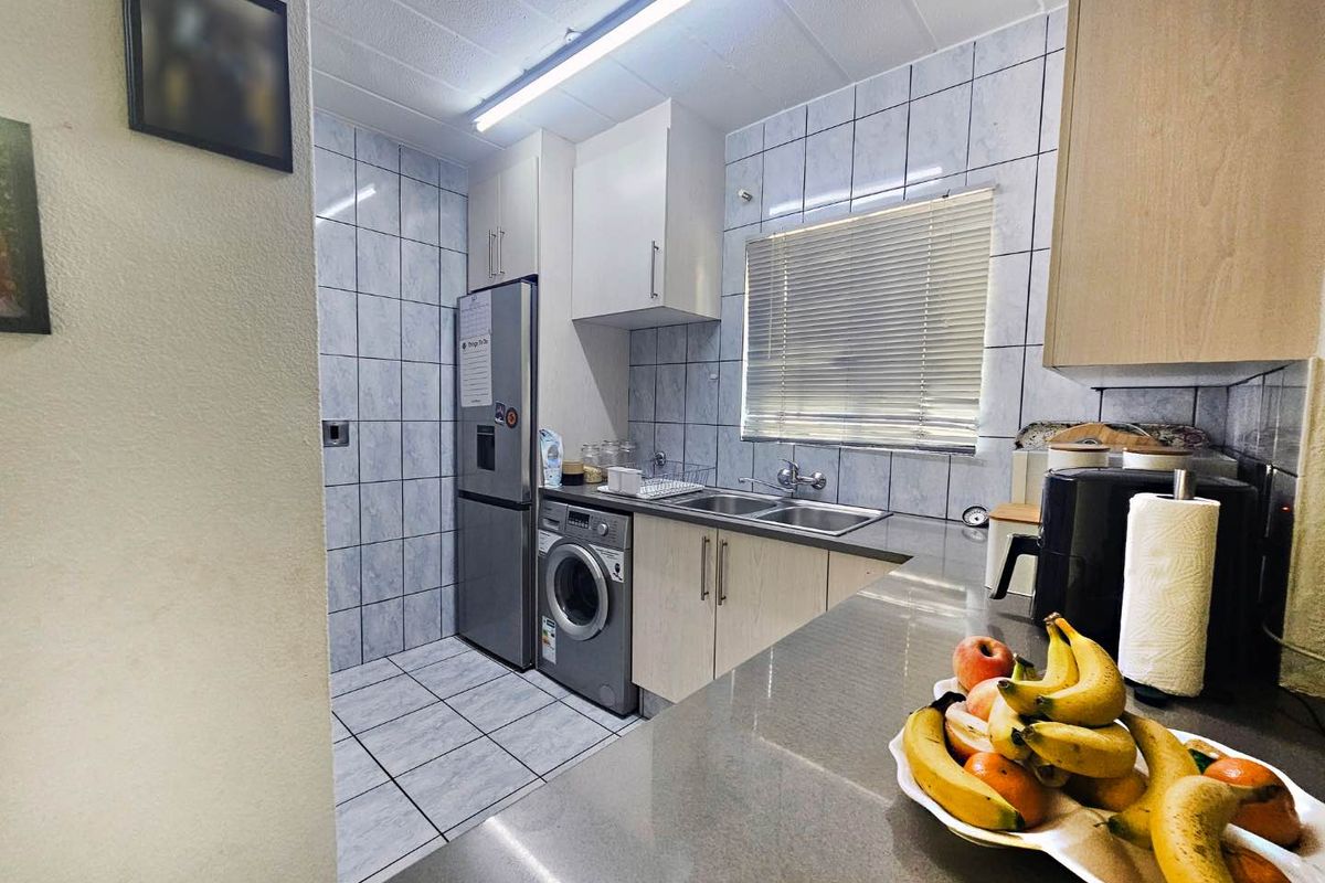 Functional kitchen featuring tiled walls and flooring, built-in cabinetry, a double basin sink, and space for integrated laundry appliances.