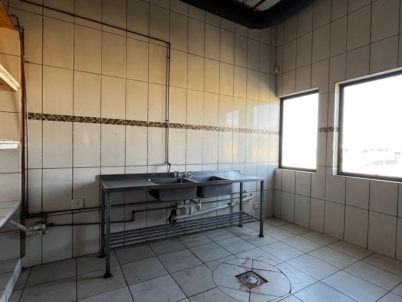Industrial scullery area featuring tiled walls, a stainless steel double sink, built-in shelving, and a floor drain.