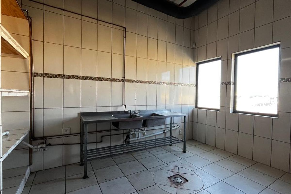 Industrial scullery area featuring tiled walls, a stainless steel double sink, built-in shelving, and a floor drain.