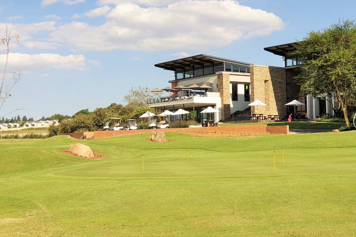 A view of the rear elevation of the building featuring stone cladding, a spacious balcony, and direct access to the landscaped golf course.