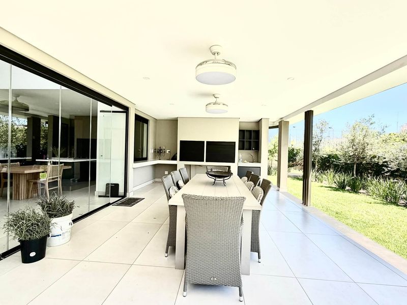 Spacious covered patio featuring a built-in braai, tiled flooring, and seamless access to the garden through large sliding glass doors.