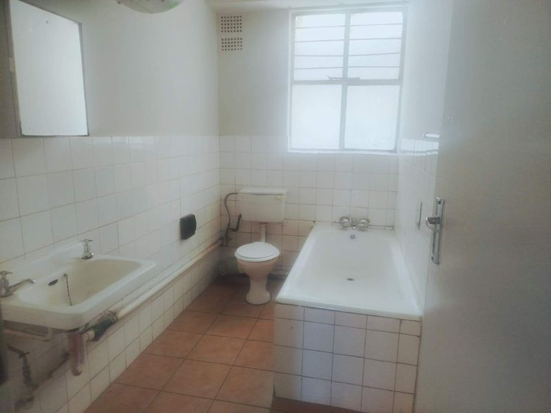 A dated bathroom featuring a built-in bathtub, pedestal washbasin, and flush toilet, finished with white wall tiles and terracotta-style floor tiles.