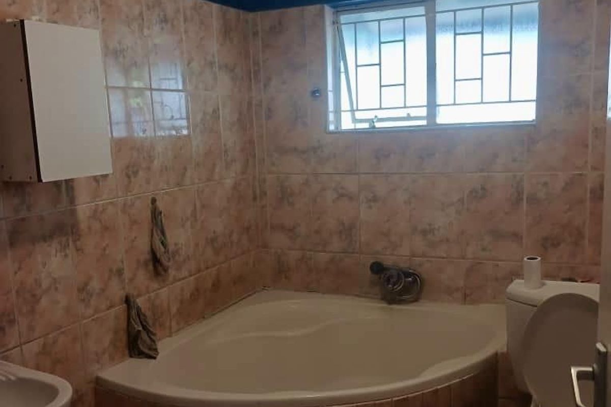 A dated bathroom featuring a corner bathtub, tiled walls, and a standard toilet, offering potential for a modern renovation.
