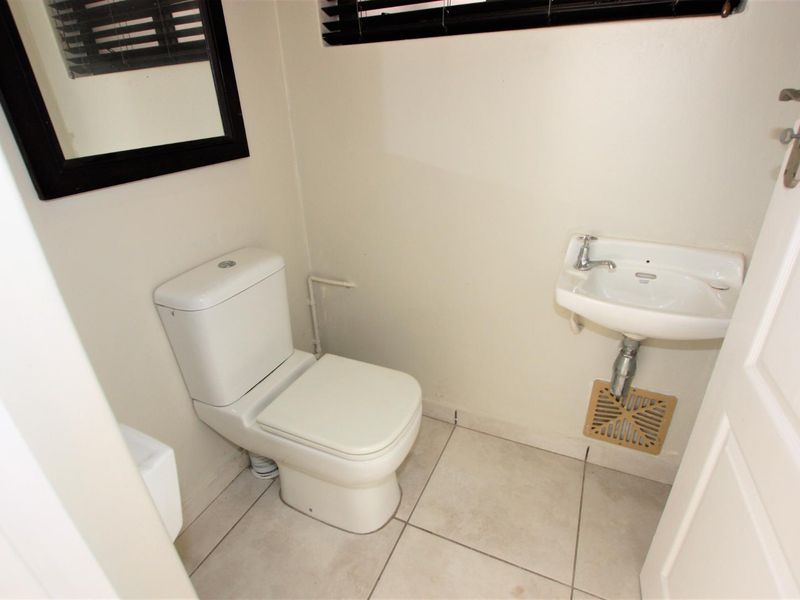 A compact guest bathroom featuring a white toilet, wall-mounted basin, and neutral floor tiles.