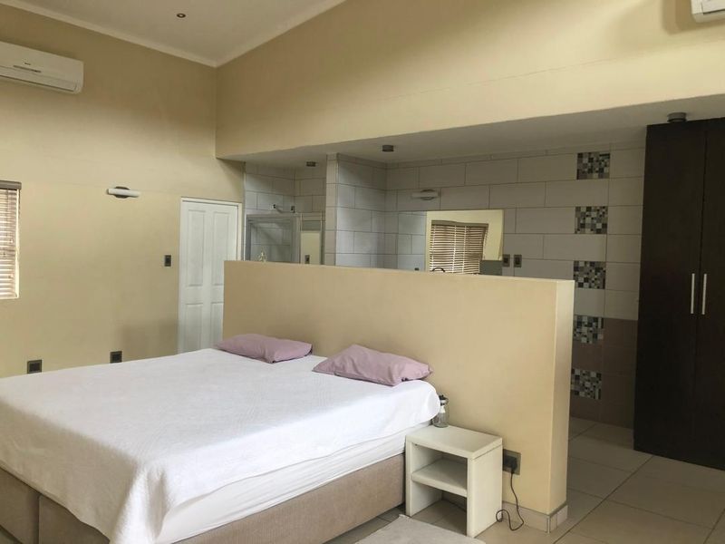 Spacious bedroom featuring an open-plan en-suite bathroom layout, built-in wardrobe, tiled flooring, and a wall-mounted air conditioning unit.