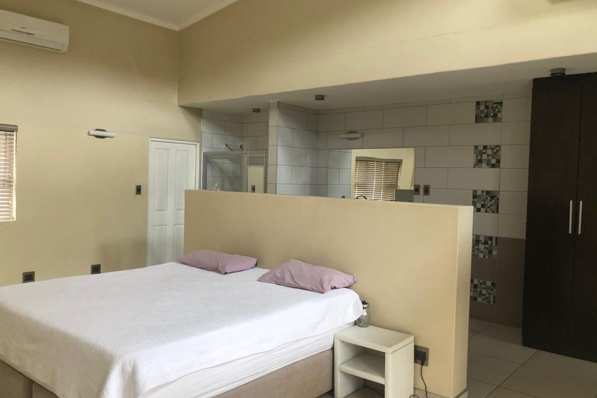 Spacious bedroom featuring an open-plan en-suite bathroom layout, built-in wardrobe, tiled flooring, and a wall-mounted air conditioning unit.