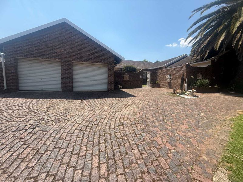 Front exterior view of the property featuring a double garage, brick facade, and a spacious brick-paved driveway.
