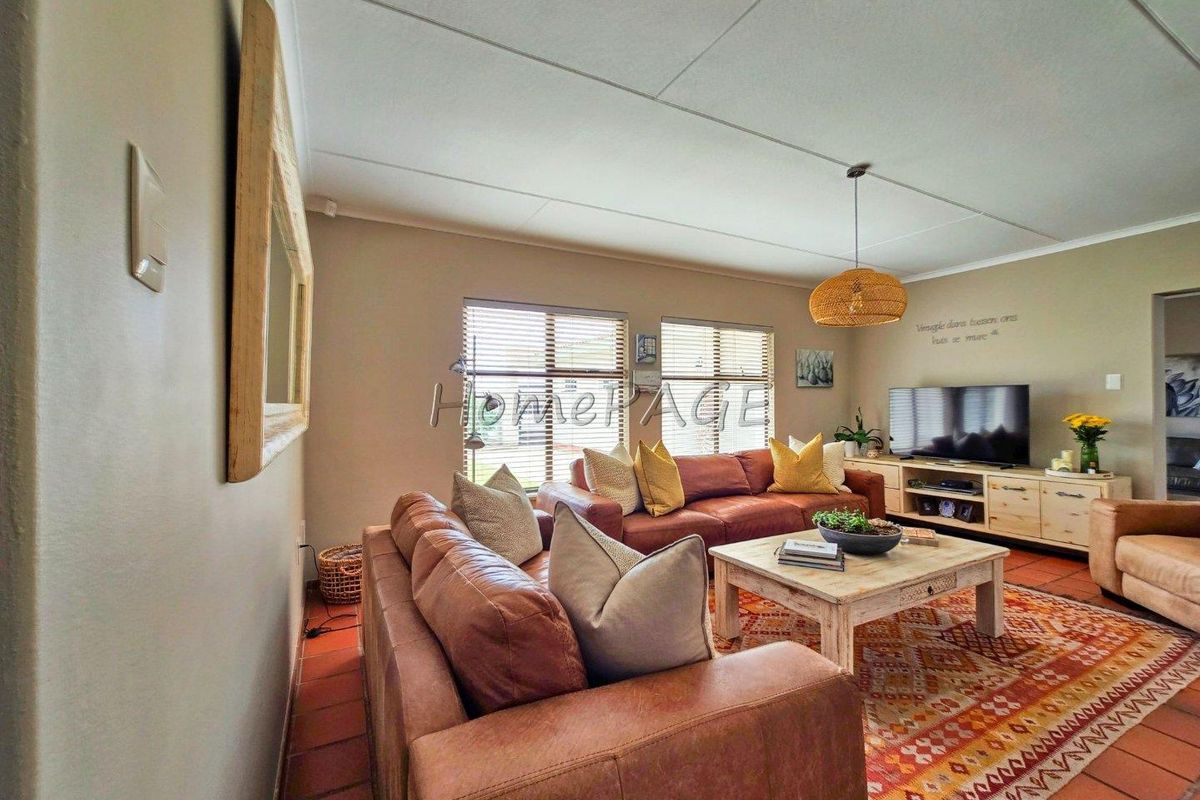 A comfortable living room featuring terracotta floor tiles, neutral wall tones, and large windows with fitted blinds, creating a warm and inviting atmosphere.