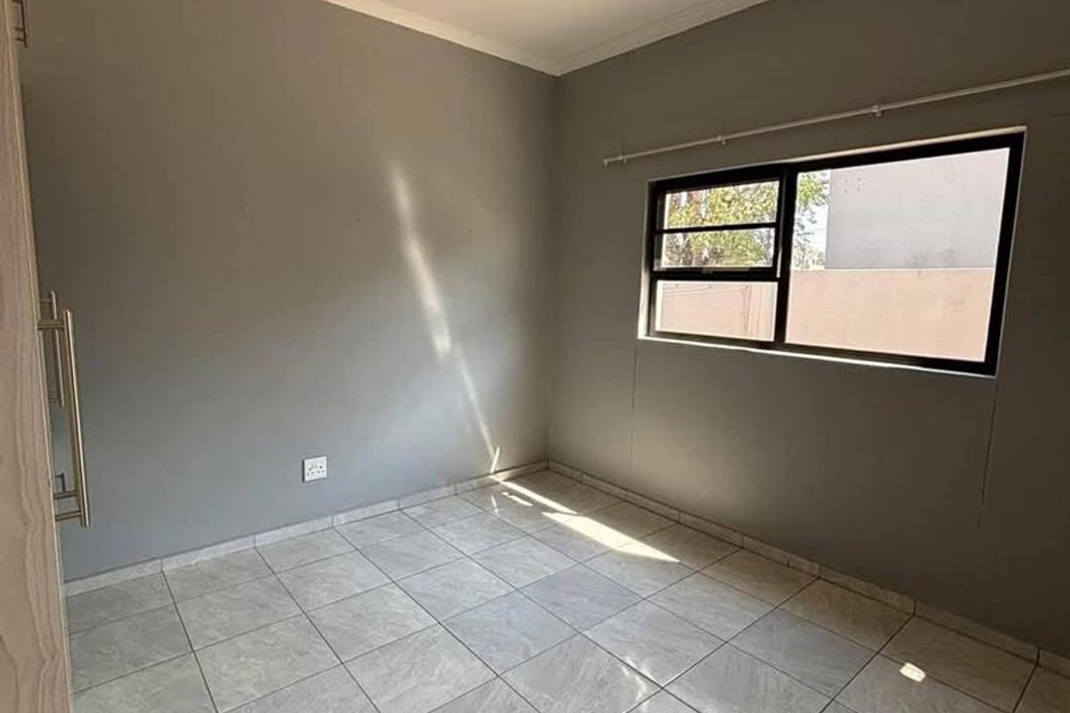 A clean, empty bedroom featuring neutral grey walls, tiled flooring, and a built-in cupboard with modern handles.
