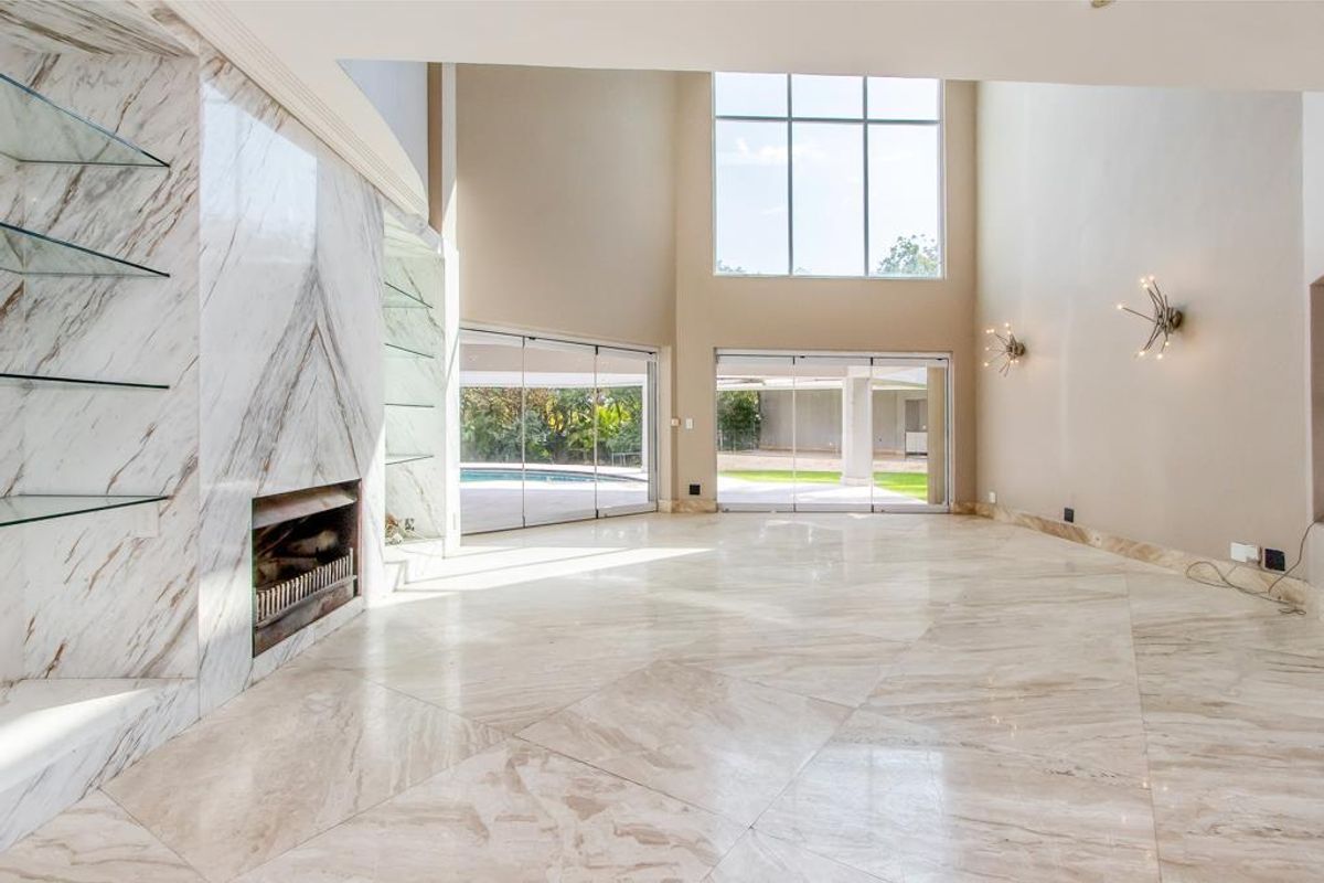 Spacious living area featuring high ceilings, large windows, marble flooring, and a built-in marble fireplace with glass shelving.