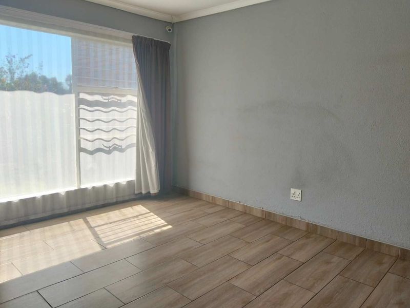 A vacant bedroom featuring wood-look tiled flooring, a large window for natural light, and neutral wall finishes.