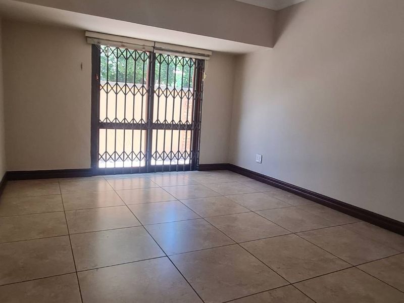 A spacious, empty bedroom featuring neutral wall tones, large format floor tiles, and a secure sliding door with an integrated security gate.