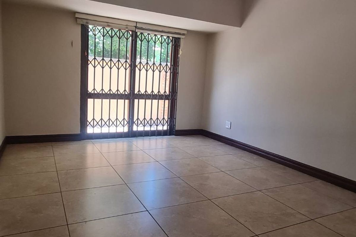 A spacious, empty bedroom featuring neutral wall tones, large format floor tiles, and a secure sliding door with an integrated security gate.