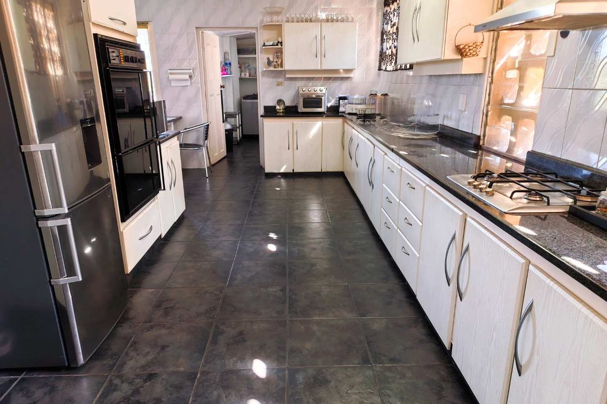A functional kitchen featuring granite countertops, built-in oven, gas hob, extractor fan, and ample cabinetry with tiled flooring and backsplash.