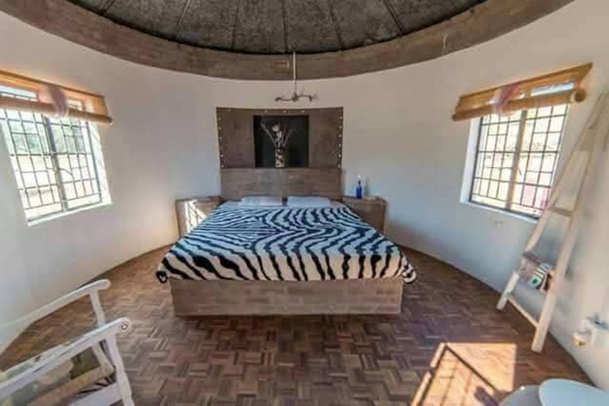 A unique circular bedroom featuring a vaulted ceiling, parquet flooring, and built-in wooden headboard with integrated bedside tables.