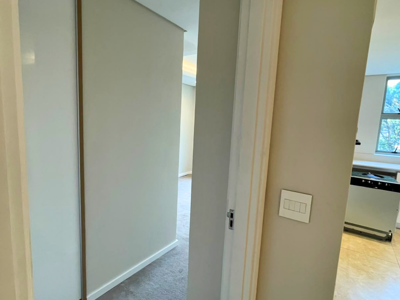 A bright hallway connecting living spaces, featuring neutral wall finishes, recessed lighting, and a mix of tiled and carpeted flooring.