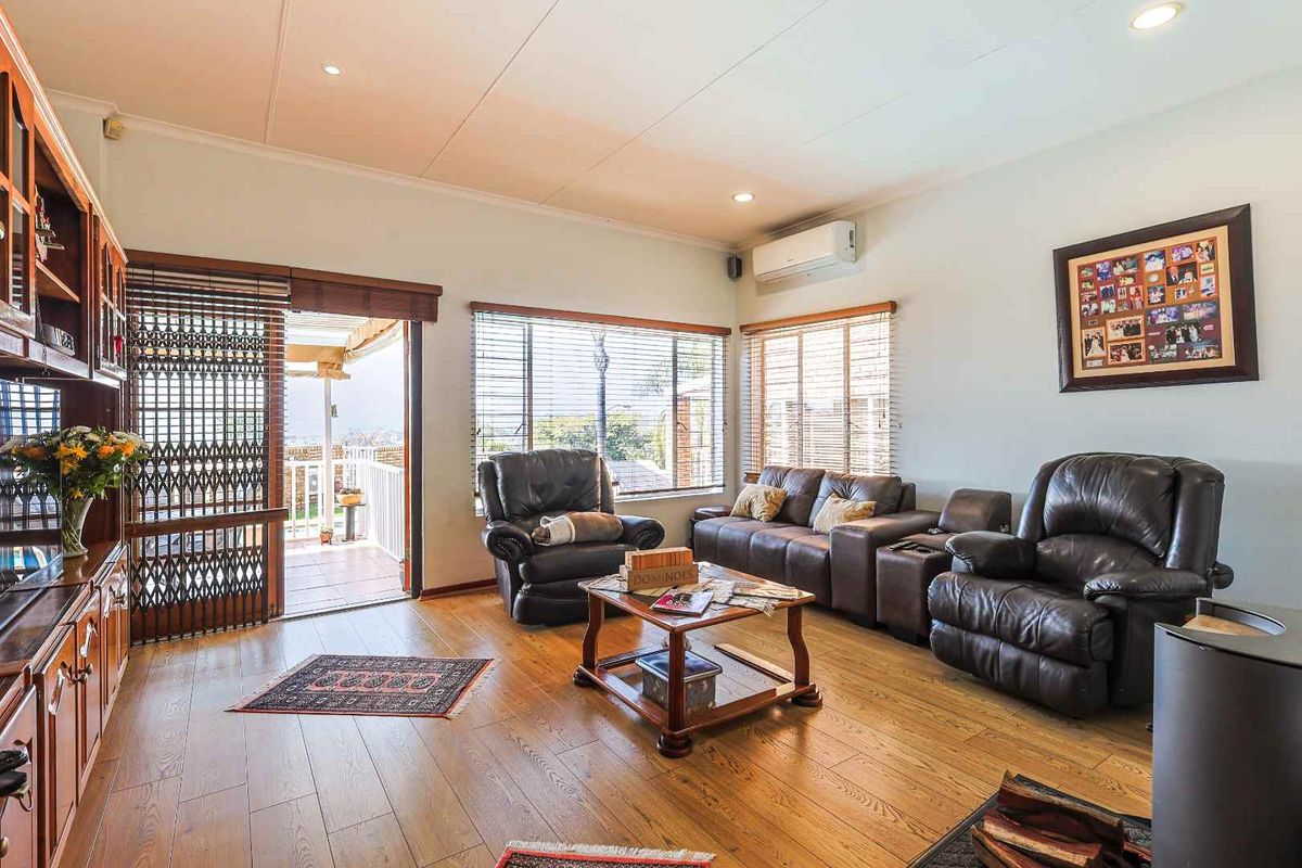 A comfortable living room featuring wood-look flooring, recessed lighting, a wall-mounted air conditioning unit, and direct access to an outdoor patio area.